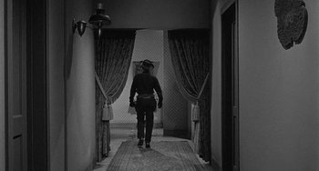 Movie still from “Terror in a Texas Town” (1958), directed by Joseph H. Lewis – A man walking down a hall way wearing a cowboy hat; Wide shot, High angle