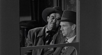 Movie still from “Terror in a Texas Town” (1958), directed by Joseph H. Lewis – A black and white photo of two men in suits and hats; Medium shot, Over the shoulder angle