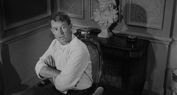 Movie still from “Terror in a Texas Town” (1958), directed by Joseph H. Lewis – Black and white photograph of a man sitting in a chair in front of a statue; Medium shot, Over the shoulder angle