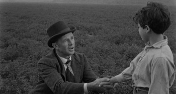 Movie still from “Terror in a Texas Town” (1958), directed by Joseph H. Lewis – An older man wearing a suit and a hat shaking hands with an older woman in a field; Medium shot, Over the shoulder angle