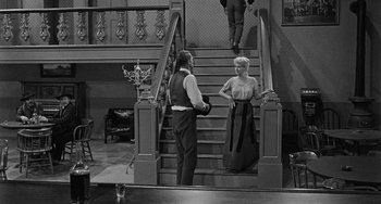 Movie still from “Terror in a Texas Town” (1958), directed by Joseph H. Lewis – A man and a woman standing at the bottom of a staircase; Wide shot, High angle