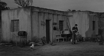 Movie still from “Terror in a Texas Town” (1958), directed by Joseph H. Lewis – A man standing in front of a building with a dog; Wide shot, High angle