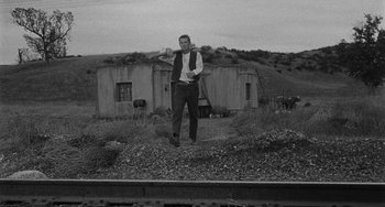 Movie still from “Terror in a Texas Town” (1958), directed by Joseph H. Lewis – A black and white photo of a man standing on the side of a train track; Wide shot, Low angle