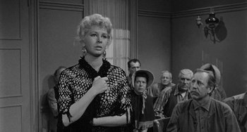 Movie still from “Terror in a Texas Town” (1958), directed by Joseph H. Lewis – A black and white photo of a woman in a courtroom; Medium shot, Over the shoulder angle