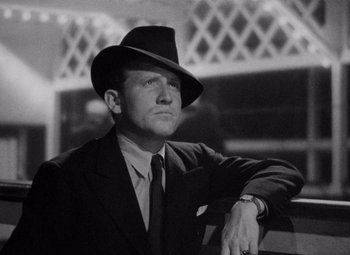 Movie still from “Test Pilot” (1938), directed by Victor Fleming – A man wearing a suit and a hat is leaning on a railing; Close Up shot, Low angle