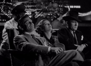 Movie still from “Test Pilot” (1938), directed by Victor Fleming – A group of people sitting on a bench in front of a crowd; Medium shot, Low angle