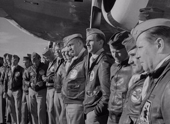 Movie still from “Test Pilot” (1938), directed by Victor Fleming – Black and white photograph of a group of men standing next to each other in front of an airplane; Medium shot, Low angle