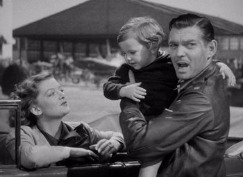 Movie still from “Test Pilot” (1938), directed by Victor Fleming – An old black and white photo of a man holding a child; Medium shot, High angle