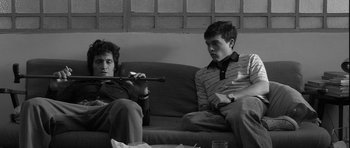 Movie still from “Tetro” (2009), directed by Francis Ford Coppola – Two young men sitting on a couch and one of them is holding a flute; Medium shot, Low angle