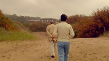 Movie still from “Tetro” (2009), directed by Francis Ford Coppola – Two men walking on a dirt road near a house; Wide shot, Over the shoulder angle
