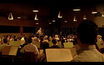 Movie still from “Tetro” (2009), directed by Francis Ford Coppola – A group of people sitting in front of a conductor; Extreme Wide shot, Over the shoulder angle