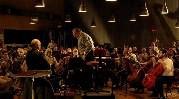 Movie still from “Tetro” (2009), directed by Francis Ford Coppola – A man standing in front of a group of people in a room; Wide shot, Low angle
