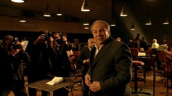 Movie still from “Tetro” (2009), directed by Francis Ford Coppola – An older man in a suit and tie standing in front of a group of people taking pictures; Medium shot, Low angle