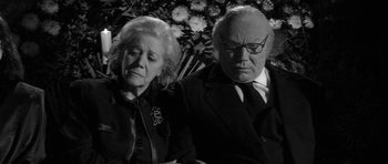 Movie still from “Tetro” (2009), directed by Francis Ford Coppola – An older man and a younger woman sitting next to each other in front of flowers; Close Up shot, Low angle