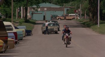 Movie still from “Tex” (1982), directed by Tim Hunter – Two people riding a motorcycle down a street; Wide shot, Over the shoulder angle