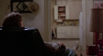 Movie still from “Tex” (1982), directed by Tim Hunter – A person sitting on a chair in a room; Wide shot, Over the shoulder angle