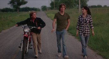 Movie still from “Tex” (1982), directed by Tim Hunter – A group of people walking down a road with a motorcycle; Wide shot, Low angle
