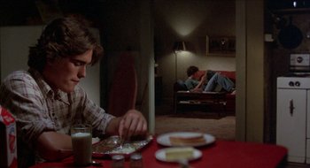 Movie still from “Tex” (1982), directed by Tim Hunter – A man sitting at a table with a plate of food; Medium shot, Over the shoulder angle