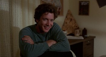 Movie still from “Tex” (1982), directed by Tim Hunter – A man sitting in front of a table smiling for the camera; Close Up shot, Over the shoulder angle