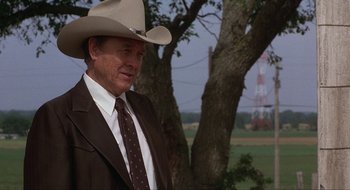 Movie still from “Tex” (1982), directed by Tim Hunter – A man in a suit and a cowboy hat standing in front of a tree; Medium shot, Over the shoulder angle