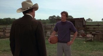 Movie still from “Tex” (1982), directed by Tim Hunter – A man holding a basketball in his hand while standing next to another man in a cowboy hat; Medium shot, Over the shoulder angle