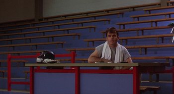 Movie still from “Tex” (1982), directed by Tim Hunter – A man sitting at a table in front of an empty lecture hall; Medium shot, Low angle