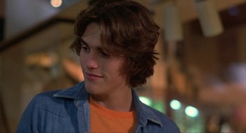 Movie still from “Tex” (1982), directed by Tim Hunter – A young man in a orange shirt is looking to his left; Close Up shot, Over the shoulder angle