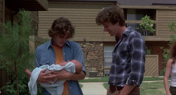 Movie still from “Tex” (1982), directed by Tim Hunter – Two young men standing next to each other holding a baby; Medium shot, Low angle