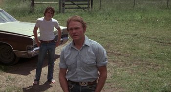 Movie still from “Tex” (1982), directed by Tim Hunter – A man standing next to another man on a dirt field; Medium shot, Low angle