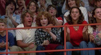 Movie still from “Tex” (1982), directed by Tim Hunter – A group of people sitting in the stands at an event; Medium shot, Low angle