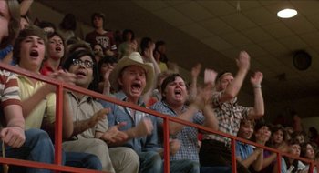 Movie still from “Tex” (1982), directed by Tim Hunter – A group of people sitting in the stands at a sporting event; Medium shot, Low angle