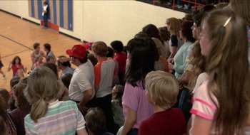 Movie still from “Tex” (1982), directed by Tim Hunter – A group of people standing in a gym watching a game; Wide shot, Over the shoulder angle