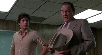 Movie still from “Tex” (1982), directed by Tim Hunter – A man in a suit holding a hat next to another man in a suit; Medium shot, Low angle