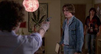 Movie still from “Tex” (1982), directed by Tim Hunter – A man holding a gun pointed at another man in a room; Medium shot, Over the shoulder angle