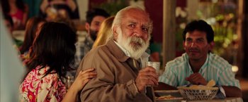 Movie still from “The 33” (2015), directed by Patricia Riggen – An old man with a beard is holding a drink; Close Up shot, Over the shoulder angle