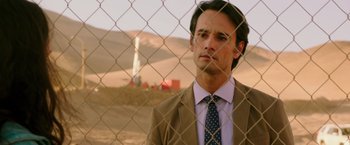 Movie still from “The 33” (2015), directed by Patricia Riggen – A man wearing a suit and tie standing in front of a chain link fence; Close Up shot, Over the shoulder angle