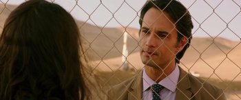Movie still from “The 33” (2015), directed by Patricia Riggen – A man in a suit and tie standing next to a woman in front of a chain link fence; Close Up shot, Over the shoulder angle