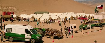 Movie still from “The 33” (2015), directed by Patricia Riggen – A group of people standing around tents in the desert; Extreme Wide shot, High angle