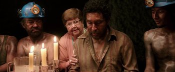 Movie still from “The 33” (2015), directed by Patricia Riggen – An older woman lighting a candle next to an older man; Medium shot, Over the shoulder angle