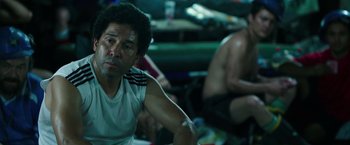 Movie still from “The 33” (2015), directed by Patricia Riggen – A person sitting in a room with other people; Medium shot, High angle