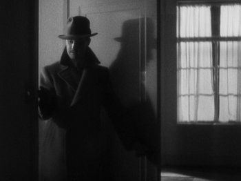 Movie still from “The 39 Steps” (1935), directed by Alfred Hitchcock – A man in a hat and a coat is looking at his cell phone; Medium shot, Low angle