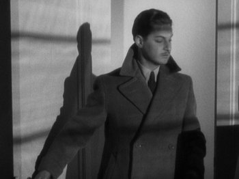 Movie still from “The 39 Steps” (1935), directed by Alfred Hitchcock – A man in a coat and tie standing in front of a window; Medium shot, High angle