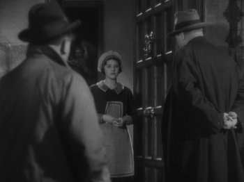 Movie still from “The 39 Steps” (1935), directed by Alfred Hitchcock – An old photo of a woman holding a book in front of two men; Medium shot, Over the shoulder angle