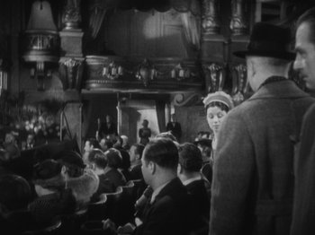 Movie still from “The 39 Steps” (1935), directed by Alfred Hitchcock – A black and white photo of people sitting in a theater; Wide shot, High angle
