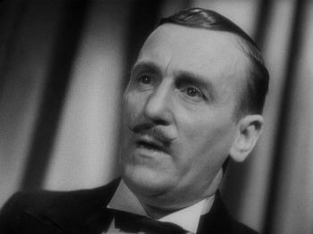 Movie still from “The 39 Steps” (1935), directed by Alfred Hitchcock – An older man wearing a suit and a bow tie; Close Up shot, Low angle