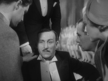 Movie still from “The 39 Steps” (1935), directed by Alfred Hitchcock – A group of people standing around a man in a tuxedo; Medium shot, High angle