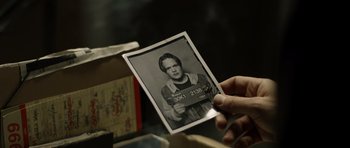 Movie still from “Department Q: The Absent One” (2014), directed by Mikkel Nørgaard – A person holding a photo of a man in a prison outfit; Close Up shot, Over the shoulder angle