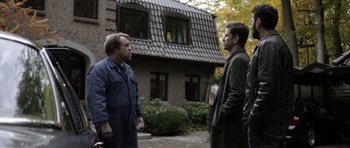 Movie still from “Department Q: The Absent One” (2014), directed by Mikkel Nørgaard – Two men standing in front of a brick house; Wide shot, Over the shoulder angle