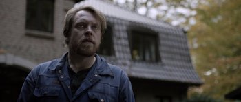 Movie still from “Department Q: The Absent One” (2014), directed by Mikkel Nørgaard – A man standing in front of a house with trees in the background; Close Up shot, Low angle