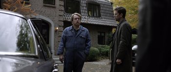 Movie still from “Department Q: The Absent One” (2014), directed by Mikkel Nørgaard – Two men standing in front of a brick house; Medium shot, Over the shoulder angle